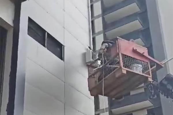 A technician in a crane performing maintenance on high-rise facade lights